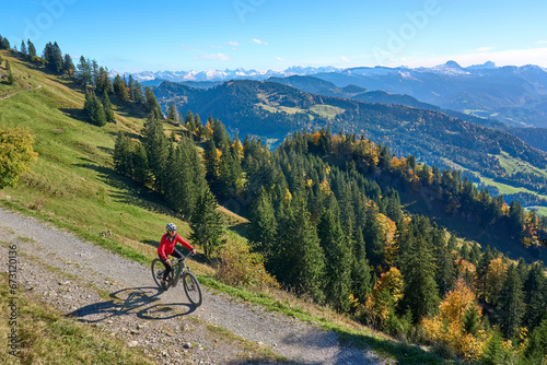 pretty senior woman riding her electric mountain bike in autumn and enjoying the spectacular view over the Allgau and Bregenz Forest alps near Steibis  Bavaria  Germany