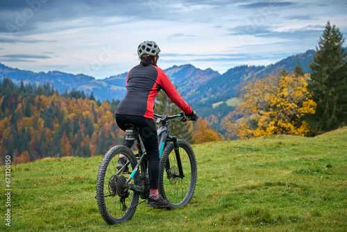 pretty senior woman riding her electric mountain bike in autumn and enjoying the spectacular view over the Allgau and Bregenz Forest alps near Steibis, Bavaria, Germany photo
