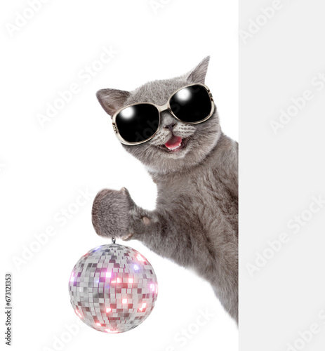 Happy cat wearing sunglasses looks from behind empty banner and shows dico ball. isolated on white background photo