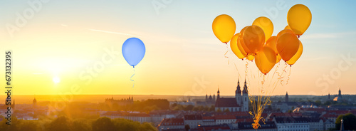 Standing out from the crowd concept. Blue balloon floating over a city separately from golden tied balloons during sunset photo