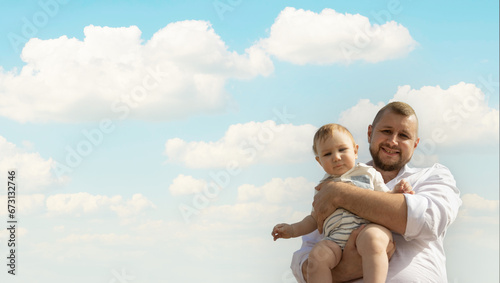 Happy father on vacation - man holding his little baby son on sky background