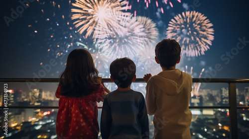 Back view of children watching big fireworks in the evening sky while standing on an open area
