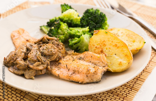 Fried river trout fillet with a complex side dish of broccoli, baked potatoes and mushroom sauce