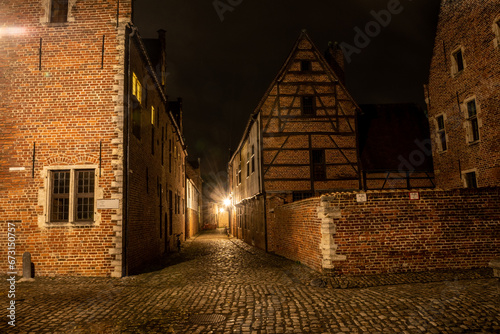 residential student houses in the Groot Begijnhof historic district of Leuven at night with streetlamp light. Atmospheric street photography showing old stone roads with pretty red brick buildings