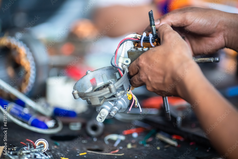 Obraz premium Selective focus to tools and hand of an electric motor repairman. Mechanic is repairing an electric motor. Electric fan motor repair work .