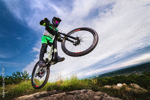 professional racer jumps on a bicycle against a blue cloudy sky. Sunny summer day. Low angle view of a man on a mountain bike jumping in the mountains