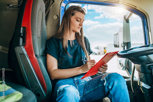 Portrait of beautiful young woman professional truck driver sitting and resting after long drive. She is writing something on notepad. Inside of vehicle. People and transportation concept.