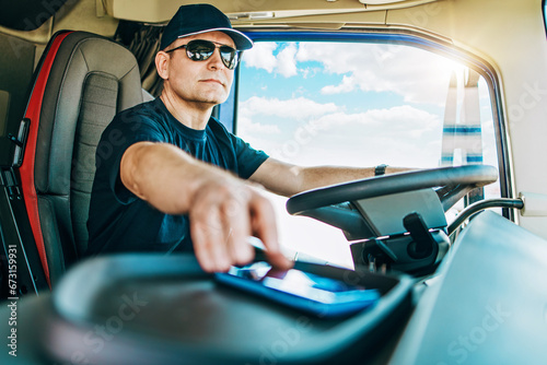 Portrait of handsome middle age man professional truck driver sitting and driving big truck. He is dangerously using his smart phone to talking with someone while driving.