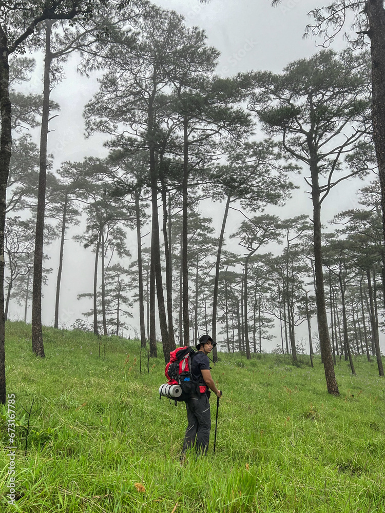 asian young man is trekking on green grass field mountain with t asian young man is trekking on green grass field mountain with t