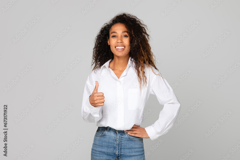 Black millennial lady showing thumbs up gesture over gray background Black millennial lady showing thumbs up gesture over gray background