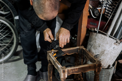 An adult male professional woodworker, carpenter, worker glues a chair, repairs, restores furniture indoors, workshop, clamping wooden products with a clamp. Close-up photography, work concept.