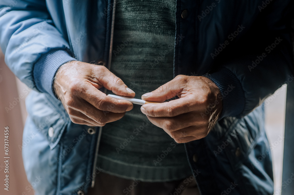 An elderly pensioner man is struggling with addiction, the desire to smoke, holding a cigarette in his hands. Medicine concept. Photography, portrait.