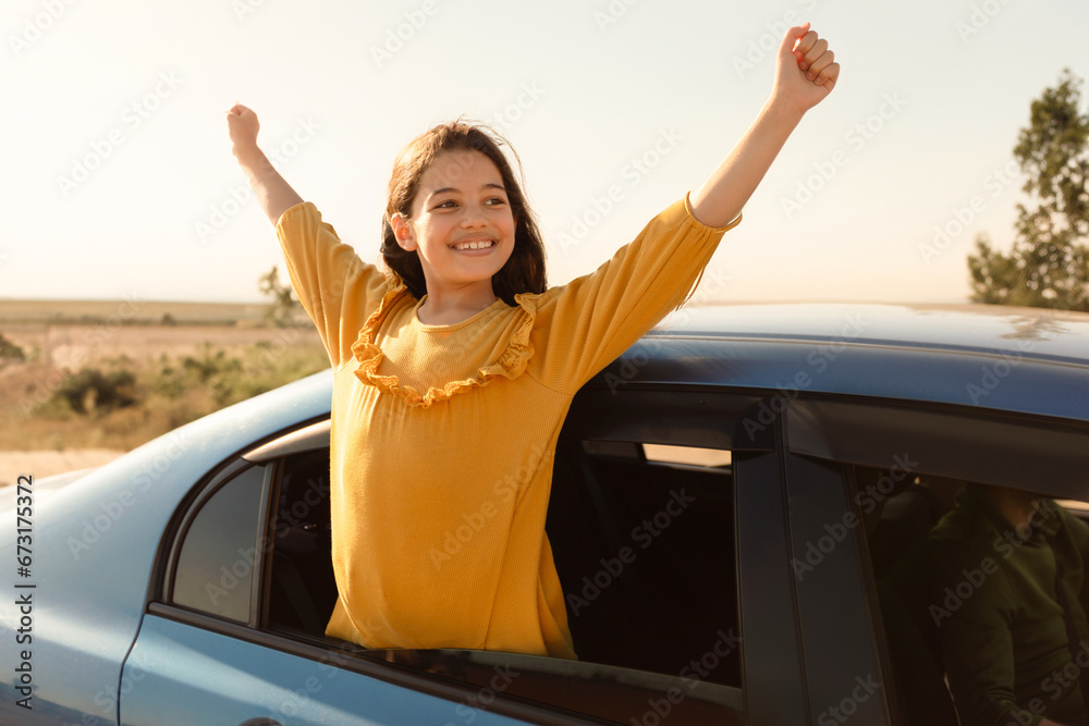 Joyful girl with arms raised from car, sunny day