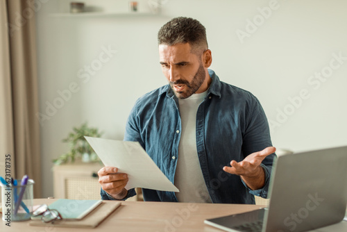 Stressed middle aged businessman holding business papers in modern office