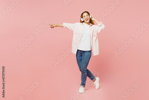 Full body young happy woman she wear shirt white t-shirt casual clothes listen to music in headphones dance have fun isolated on plain pastel light pink background studio portrait. Lifestyle concept. photo