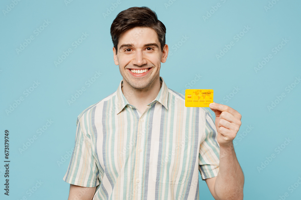 Young happy cheerful smiling man he wears striped shirt casual clothes hold in hand mock up of credit bank card isolated on plain pastel light blue cyan background studio portrait. Lifestyle concept. Young happy cheerful smiling man he wears striped shirt casual clothes hold in hand mock up of credit bank card isolated on plain pastel light blue cyan background studio portrait. Lifestyle concept.
