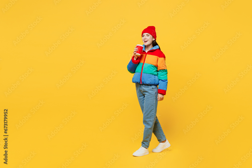 Full body young fun woman she wears padded windbreaker jacket red hat casual clothes hold takeaway delivery craft paper cup coffee to go isolated on plain yellow background studio. Lifestyle concept. Full body young fun woman she wears padded windbreaker jacket red hat casual clothes hold takeaway delivery craft paper cup coffee to go isolated on plain yellow background studio. Lifestyle concept.