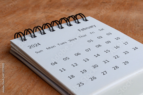 February 2024 white table calendar on wooden background. Calendar concept. photo