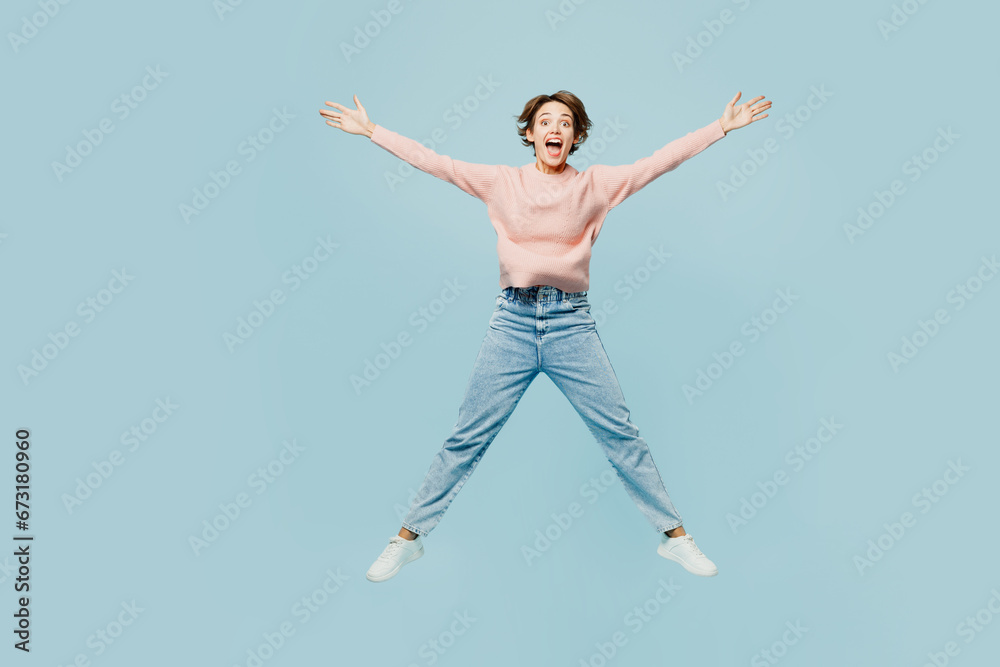 Full body young excited overjoyed happy woman wear beige knitted sweater casual clothes jump high with outstretched hands legs isolated on plain pastel light blue cyan background. Lifestyle concept.
