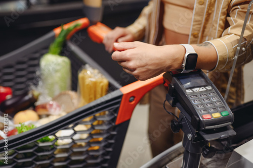 Close up cropped shot photo customer holding wireless bank terminal process acquire smart watch payment shopping at supermaket store grocery shop buy products in hypermarket. Purchasing food concept.