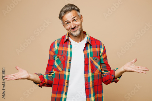 Adult sad man he wear red shirt white t-shirt casual clothes shrugging shoulders looking puzzled spread hands isolated on plain pastel light beige color background studio portrait. Lifestyle concept.