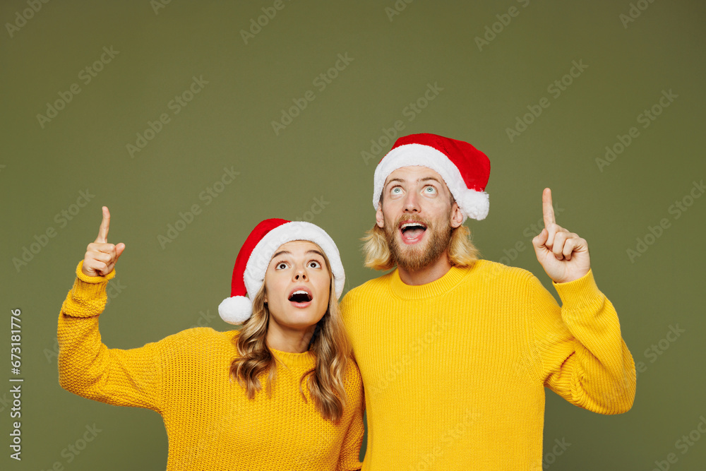 Merry shocked fun young couple two friends man woman wearing sweater Santa hat posing point index finger overhead on area isolated on plain green background. Happy New Year Christmas holiday concept. Merry shocked fun young couple two friends man woman wearing sweater Santa hat posing point index finger overhead on area isolated on plain green background. Happy New Year Christmas holiday concept.