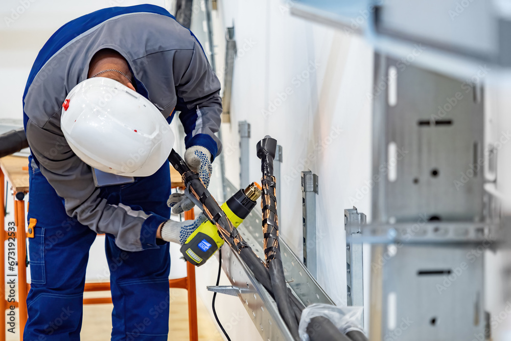 Cabling work. Man electrician installer. Guy in helmet is doing cabling. Uses heat gun for