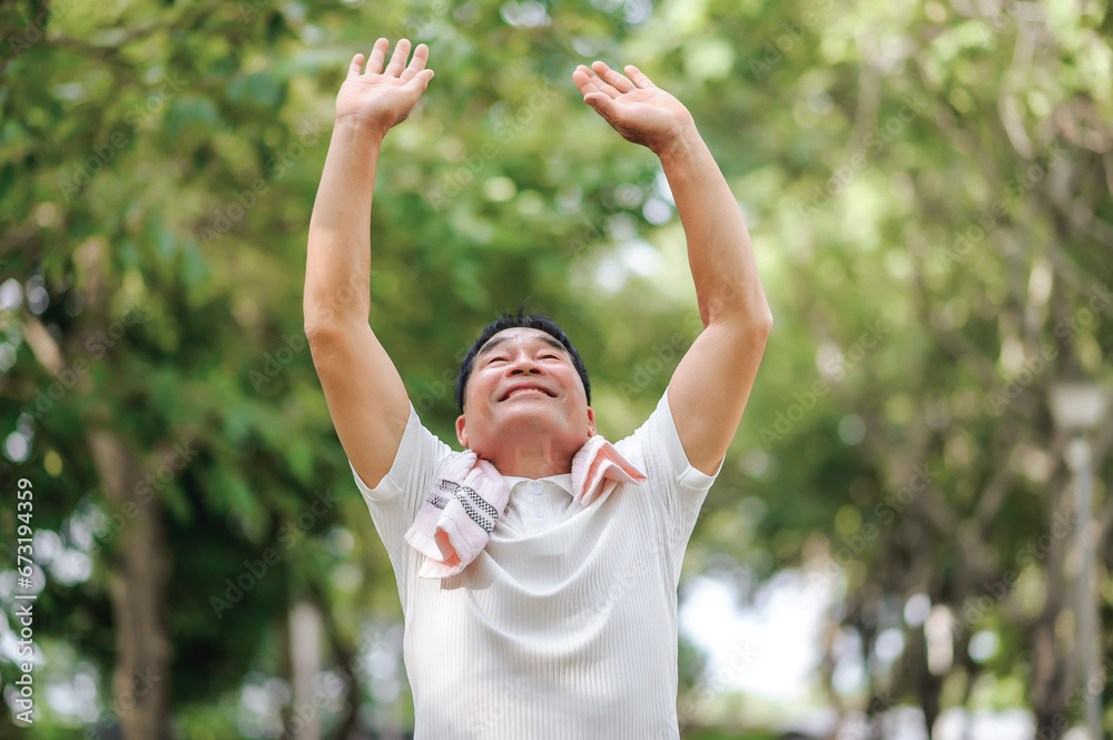 An elderly man stretched his arms high while breathing fresh air in a natural green park and refreshed after taking a deep breath of fresh air.