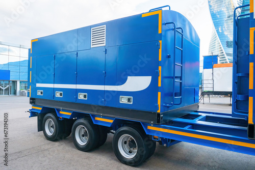 Container for transporting equipment. Blue semi-trailer on wheeled platform. Container transporting backup power source. Blue container for transporting transformer. Industrial transport technologies