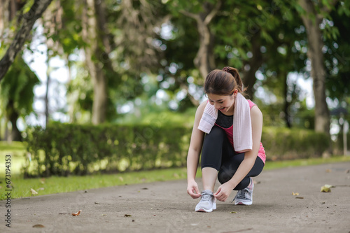 An Asian Woman Is Tying Shoelaces With A Kind Face And A Gentle Smile In The Park Is Full Of Trees. Looks Around The Park and Smiles While Feels Happy And Alive