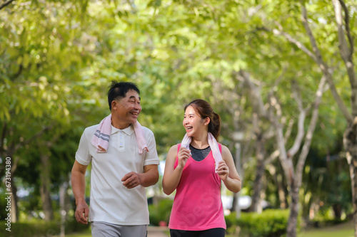 Asian Elderly Father and Daughter are jogging and relaxing in a green park, Breathing in the fresh air and enjoying the beautiful scenery. Health care and family bonding.