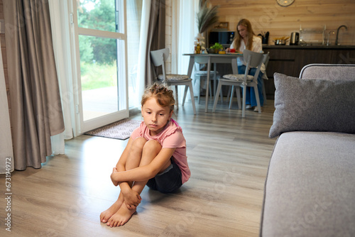 Upset little girl lonely sitting on floor in living room