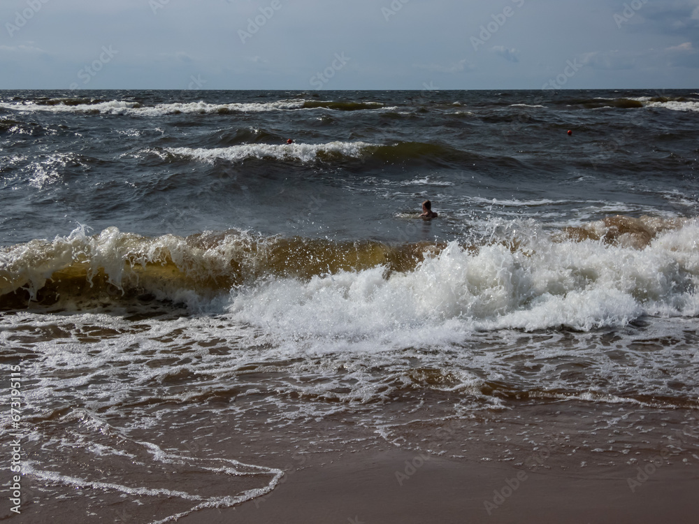 Seascape of the Baltic sea with big foamy waves in windy day with brown sand on the shore and blue sky above in sunlight