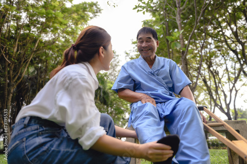 Daughter takes care to foot massage her father, Encourage him during his illness in hospital garden. The happiness of old adult patients while rehabilitation or physical therapy of retired patients. © kokliang1981
