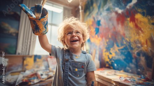 A joyful little boy stands within a house, clutching a paint bucket, and enthusiastically participating in a DIY home renovation project, adding a creative and playful element to the endeavor