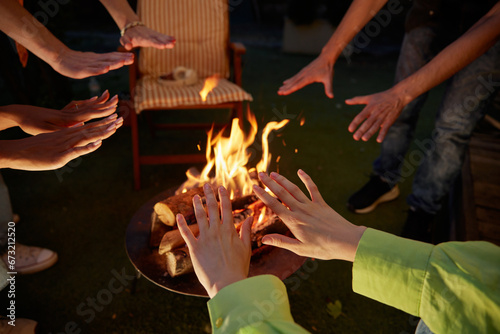 Group of young people warming hands over burning campfire closeup