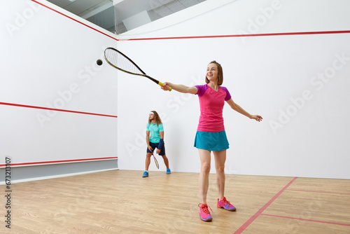 Happy millennial-age couple characters playing game of racquetball together photo