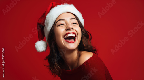 Joyful woman wearing a Santa hat  laughing against a vibrant red background  embodying the festive spirit of Christmas.