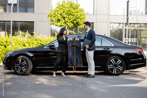 Female chauffeur gives a businessman his suit, after a business trip in luxury taxi. Concept of personal assistant, driver and business transportation service