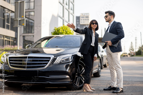 Business partners have a conversation while standing together near luxury car outdoors. Female driver showing way for a businessman arriving to destination © rh2010