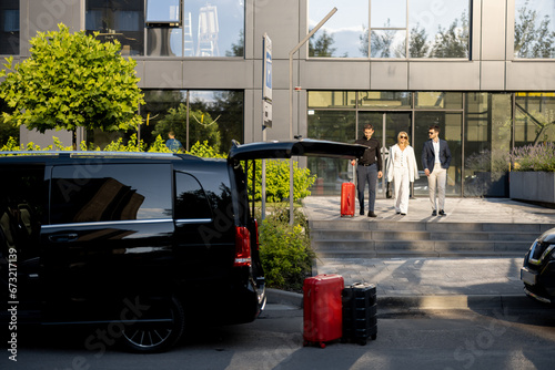 Driver or concierge helps a business couple carry their suitcases to the office or hotel from a minivan taxi. Concept of business travel and transportation service photo