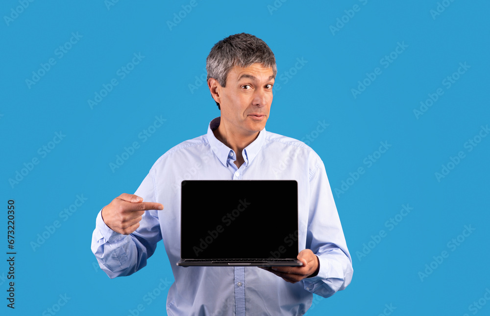 Mature businessman showing laptop pointing at empty monitor screen, studio Mature businessman showing laptop pointing at empty monitor screen, studio