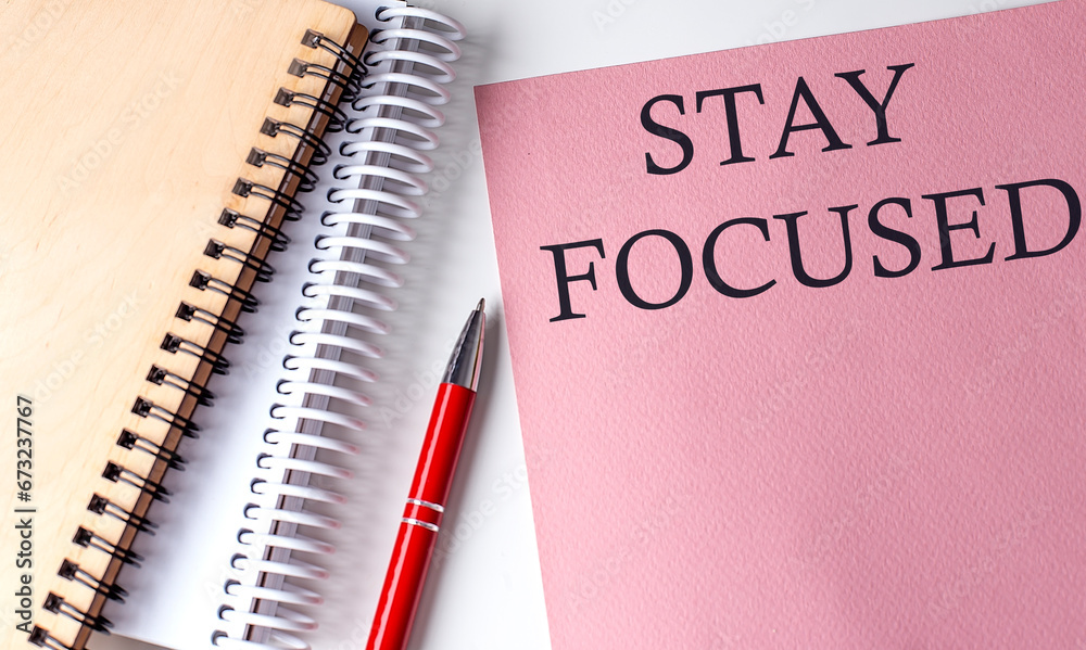STAY FOCUSED word on the pink paper with office tools on white background STAY FOCUSED word on the pink paper with office tools on white background