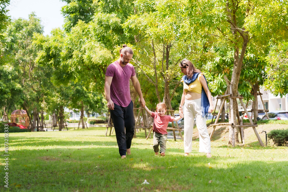 Fototapeta premium Adorable Caucasian boy is playing with his father and mother in the village grass. father with a mustache and beautiful mother, son walk hand in hand at the park. family vacation Concept