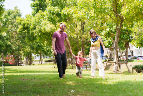 Adorable Caucasian boy is playing with his father and mother in the village grass. father with a mustache and beautiful mother, son walk hand in hand at the park. family vacation Concept