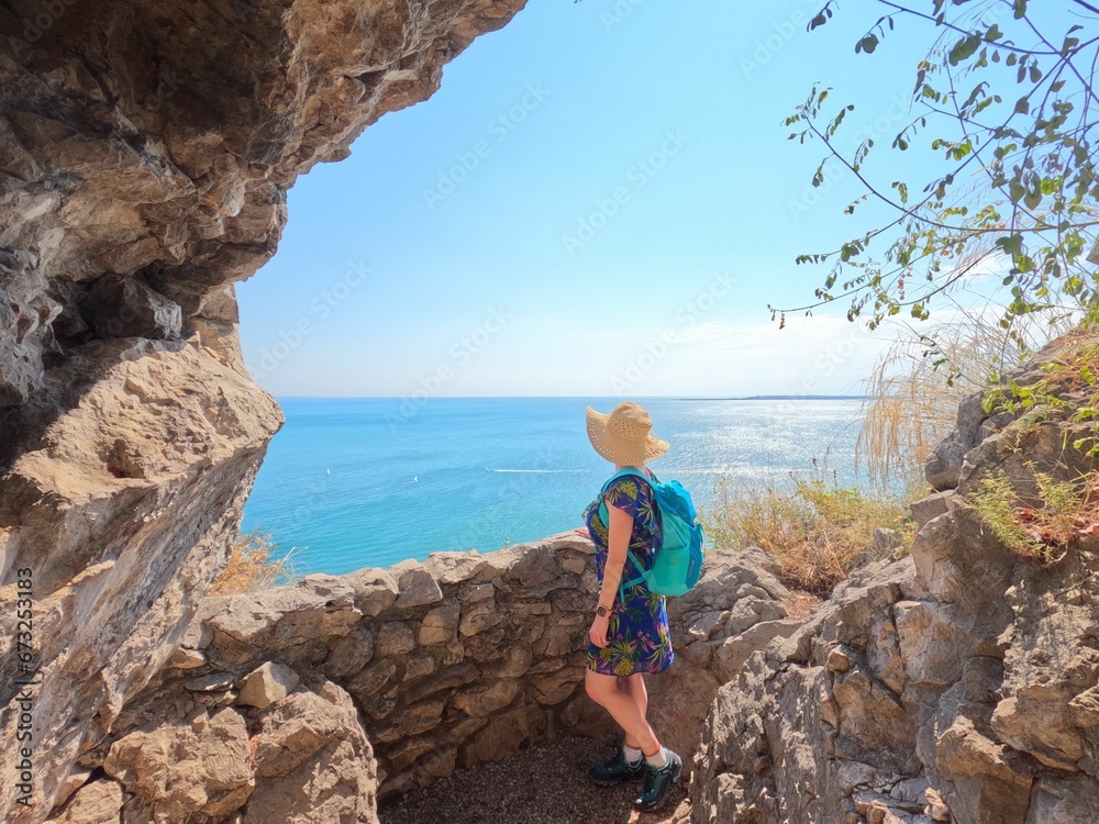 Young woman wearing a blue backpack and a hat admiring the sea view in rilkeweg, italy