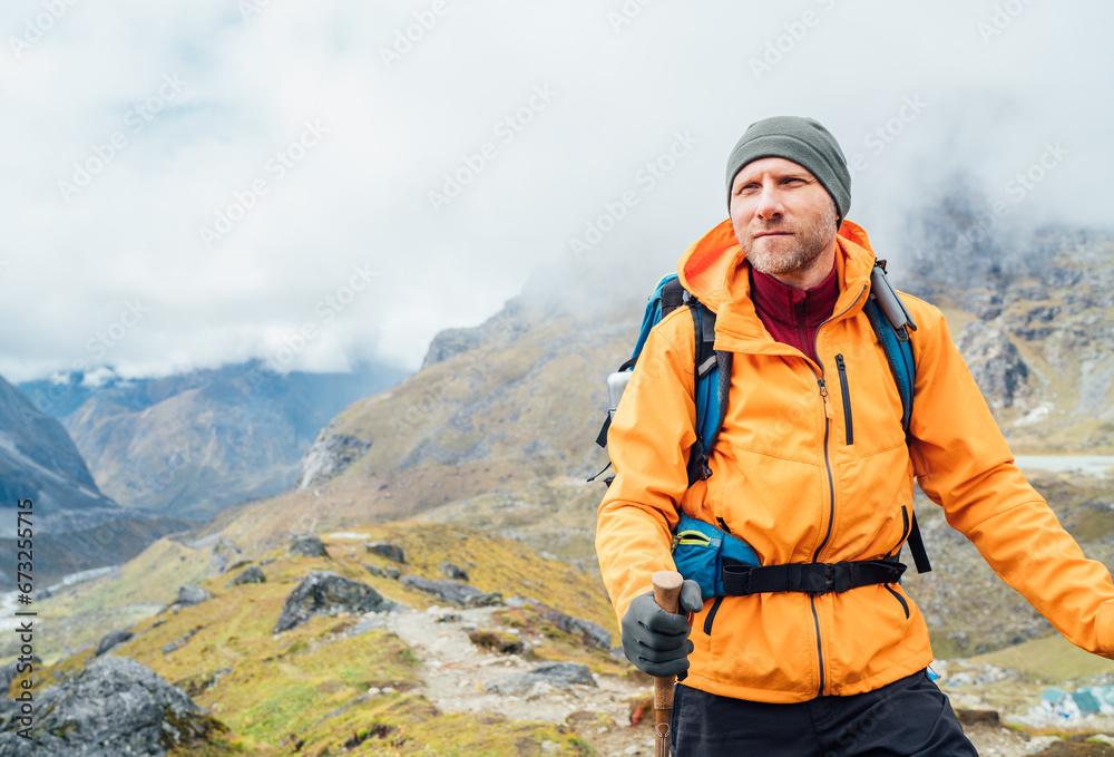 Fototapeta premium Portrait of caucasian man with backpack and trekking poles in Makalu Barun Park route near Khare. Mera peak climbing acclimatization active walk. Backpacker enjoying valley view. Active people concept