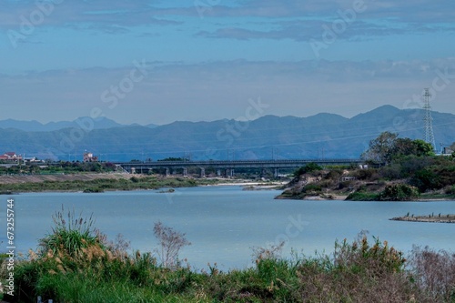 Scenic view of a river with mountains and a bridge in the background.