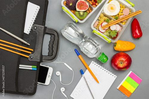 Black briefcase with phone and headphones. Bottle of water, notebooks with pens, lunch box of fruits, berries and nuts