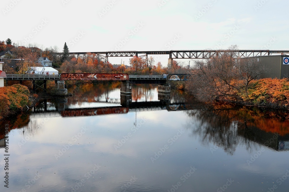 Steel bridge arches over a river surrounded by lush autumn trees